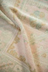 A fold reveals the soft, hand-knotted pile and even wear of a distressed Oushak carpet.