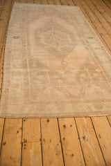 Angled perspective of a vintage Oushak runner showing its length and soft, abrashed ground in sand and blush.