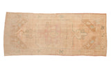 Vintage distressed Oushak rug runner with a large central medallion in soft tones of ivory, pink, and pale turquoise.