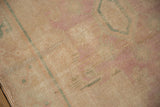 Detailed texture of a distressed rug showing worn knot heads in coffee, pink, and pale green.