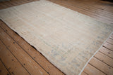 Distressed vintage Oushak rug with worn beige pile, intact side selvage, and subtle patterns.