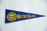 Gold 'Notre Dame' text and partial crest on vintage blue felt pennant.