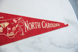 Cream 'North Carolina' lettering on red vintage felt pennant, showing textured surface and worn tip.
