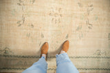 Distressed vintage Oushak carpet with worn texture, faded mint green vinery on cream.
