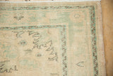 Distressed vintage Oushak rug corner, showing mint green border motifs and worn ivory pile.