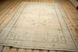 Secured end of a distressed Oushak rug, showing worn ivory pile, mint and pale brown motifs.