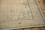 Distressed Oushak rug corner with mostly even wear, ivory tones, and muted green motifs.