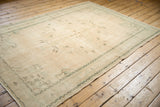 Distressed Oushak carpet edge with faded mint green border and visible wear.