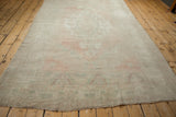 Long view of distressed vintage Oushak carpet, showing faded pale pink and sea foam green.