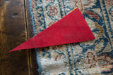 Vintage red felt pennant close-up, showing blue edge stitching on a patterned rug.