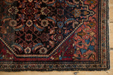 Corner detail of a vintage Farahan Sarouk rug showing its cranberry spandrel with scrolling arabesques.