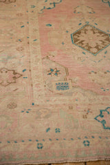 Close-up of geometric floral medallions in aqua, brown, and dusty rose on a distressed Turkish Oushak.