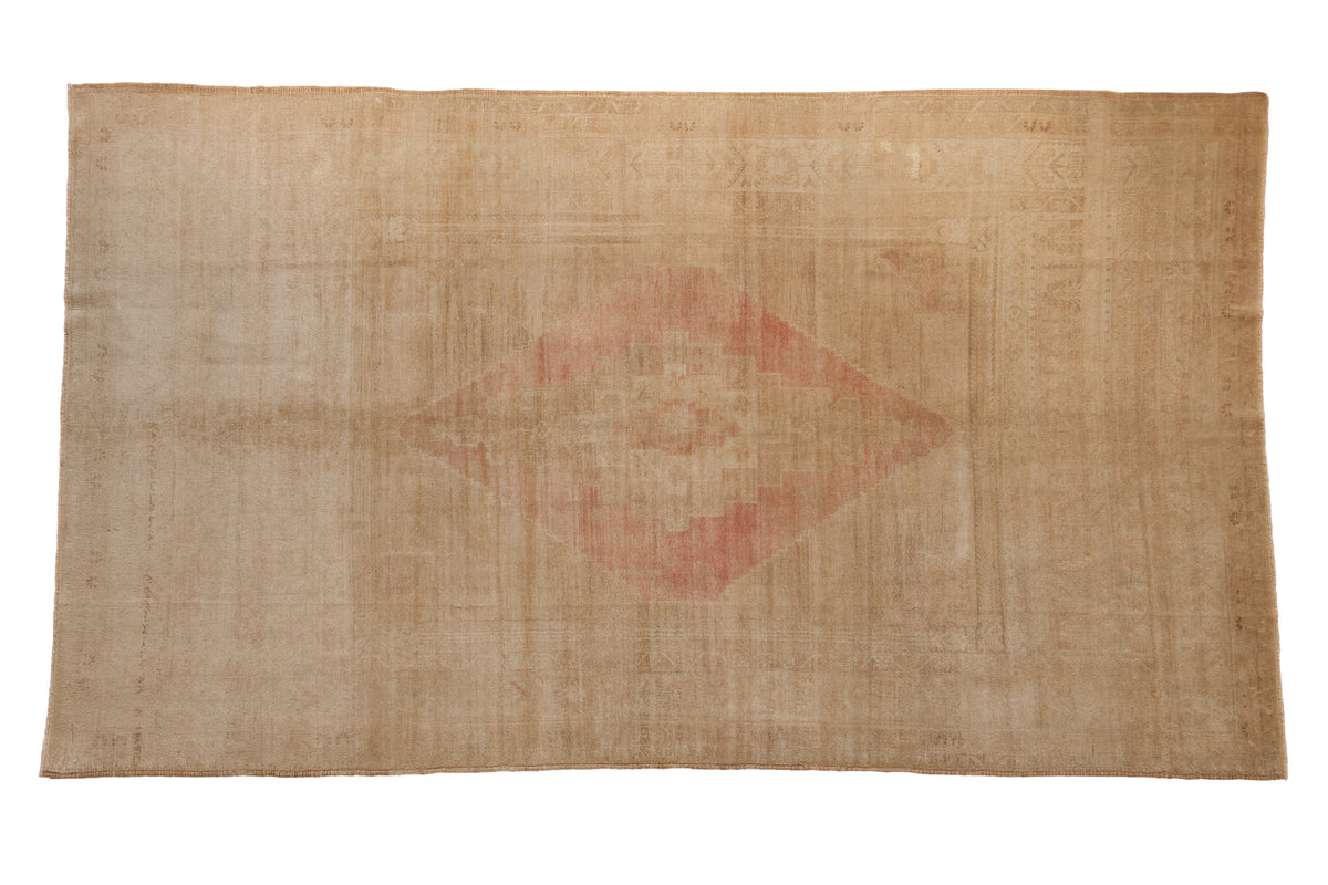 Vintage distressed Oushak carpet with a dusty blush stepped medallion on a neutral sand and ivory field.