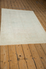 Vintage distressed Oushak rug shown at an angle, featuring an evenly worn pile in muted cream tones.