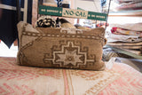 Close-up of vintage hand-knotted pillow showing textured geometric pattern in brown, tan, and cream.