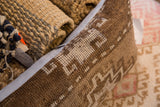 Side view of the vintage Turkish rug fragment pillow, featuring brown and beige geometric knotting with light blue piping.