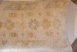 Close-up of vintage hand-knotted rug fragment pillow, showing textured cream pile and faded geometric motifs.