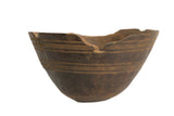 Vintage African wooden bowl with a dark finish, carved horizontal lines, and a rustic chipped rim.