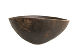 A primitive hand-carved African wooden bowl with a dark, textured finish and visible character.