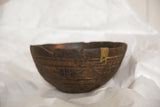 Aged metal repair and visible cracking on the rim of a hand-carved wooden bowl.