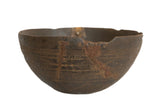 Primitive vintage African wooden bowl, dark brown with carved patterns, cracks, and storied repairs.