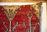 Angled close-up of hand-knotted Oushak rug fragment pillow, rich red and gold geometric motifs.