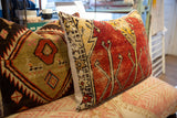 Red vintage rug fragment pillow side with stylized motifs, next to geometric pattern.