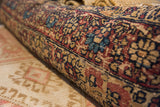 Rolled antique Kerman fragment, detailed red, blue, and beige pattern, exposed foundation.