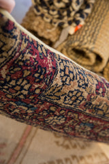 Pillow edge showing aged Kerman rug fragment texture in traditional red, blue, and beige.