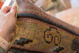 Hand holding vintage Khotan rug fragment pillow, showing its hand-knotted texture and muted geometric pattern.