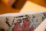 Hand-knotted pile detail on the side of a vintage rug fragment pillow in beige, black, and coral.