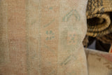 Detail of vintage rug fragment pillow with hand-knotted faded beige and teal Oushak pattern.