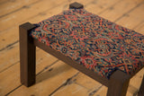 Angled close-up of the antique rug footstool's Persian Herati pattern and dark wood leg.