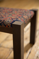 Corner detail of the footstool's solid wenge wood leg and antique rug fragment top.