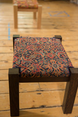 Two antique rug fragment footstools in a row, with dark wood legs and Herati pattern tops.