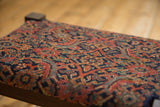 Angled close-up of the intricate hand-knotted Herati pattern on the antique rug footstool.