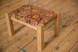 Colorful antique rug fragment footstool on an oak frame, shown from a high three-quarter angle.