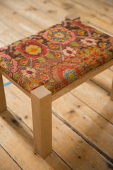 A solid oak leg meets the textured, colorful antique rug fragment seat of a reclaimed footstool.
