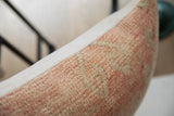 Textured edge of vintage rug fragment pillow, showing muted peach and natural fibers.