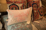 Textured surface of a vintage rug fragment pillow, faded pink and beige.