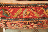 Close-up of vintage rug pillow's textured pile, with red, teal, and gold tribal motifs.