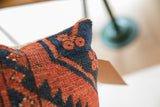 Vintage rug fragment pillow with coarse texture, deep blue, and reddish geometric patterns.
