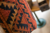 Close-up of vintage rug fragment pillow, hand-knotted with terracotta, navy, and tan geometric patterns.