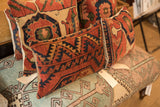 Group of vintage rug fragment pillows with rust, blue, and tan geometric patterns.