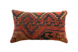 Hand-woven vintage rug fragment pillow in burnt orange, navy, and tan geometric patterns.