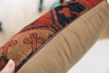 Vintage rug fragment pillow, detailed hand-knotted red, blue, orange texture, plush beige side.