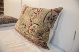 Corner of oversized vintage rug pillow with intricate red, blue, and gold mythological motifs.