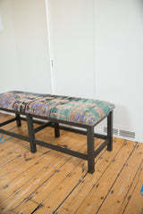 Profile view of the long vintage rug bench, showing its dark wood frame and patterned textile seat.