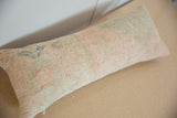 Distressed Oushak rug fragment texture, featuring faded peach, green, and blue tones, with zipper.