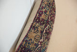 Vintage rug fragment pillow edge with aged red, blue, and tan hand-knotted pattern.